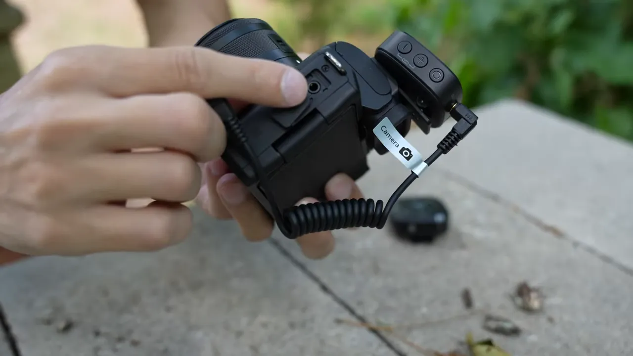 Maono WM820 receiver connected to a camera via a coiled cable showing control buttons