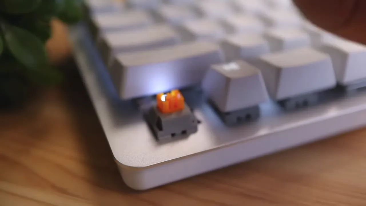 Close-up of an exposed orange mechanical switch on the white keyboard with white backlight underneath