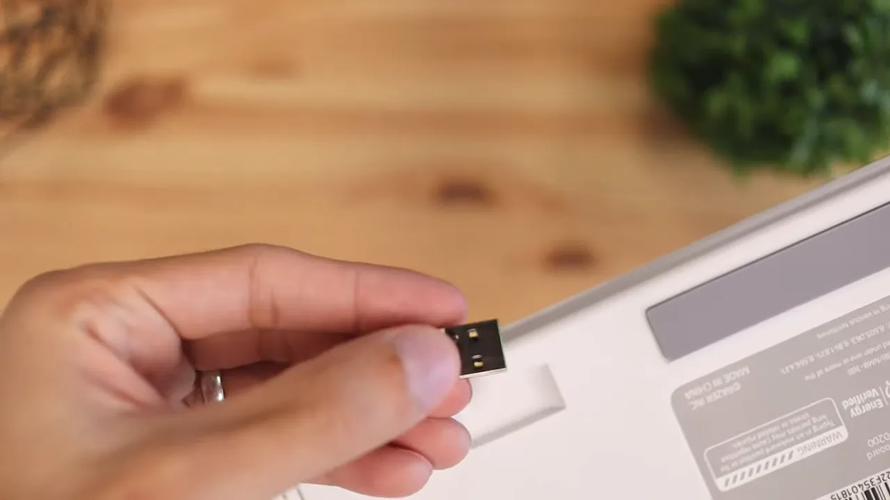 Hand holding a small USB wireless dongle removed from the underside of the keyboard