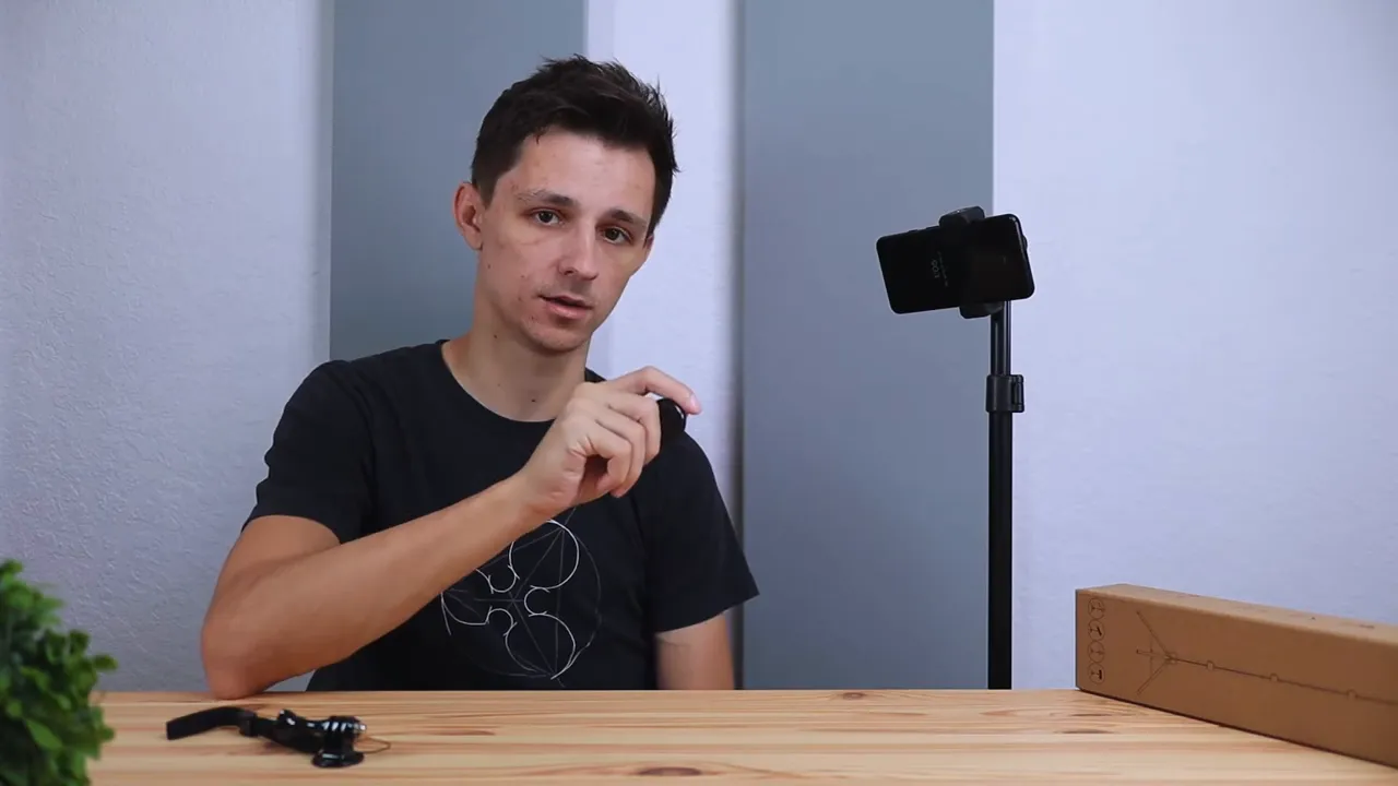 Presenter holding a Bluetooth remote in front of Ruittos tripod and boxed tripod on table