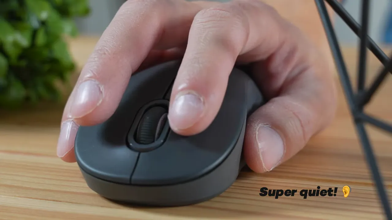 Close-up of a finger pressing the Logitech Signature M550 mouse on a wooden desk with the overlay text 'Super quiet!' in the lower right.