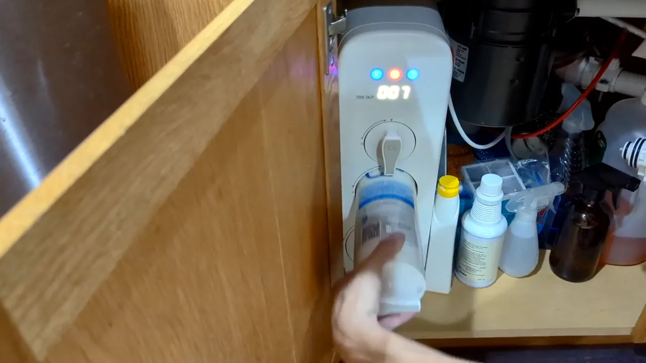 Hand pulling the CF (center) cartridge out of a Waterdrop G3 reverse osmosis unit installed under a sink.