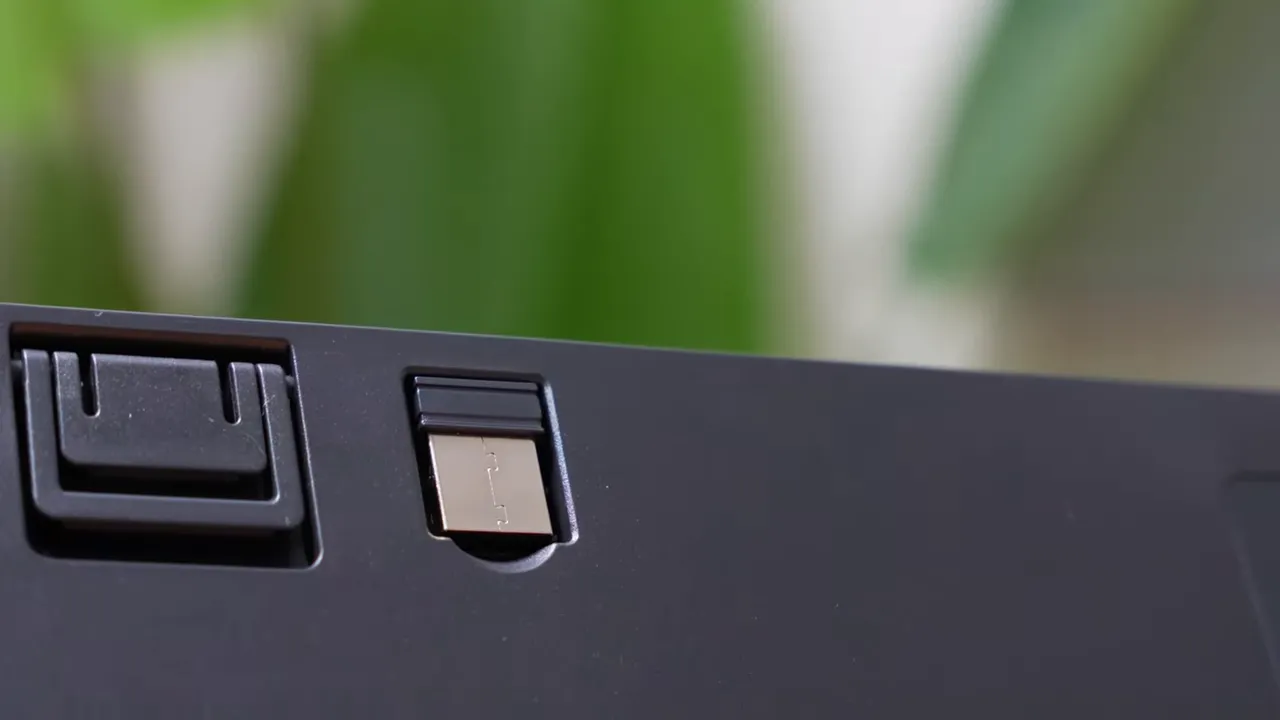 keyboard underside showing USB wireless dongle stored in its slot next to an adjustable folding foot