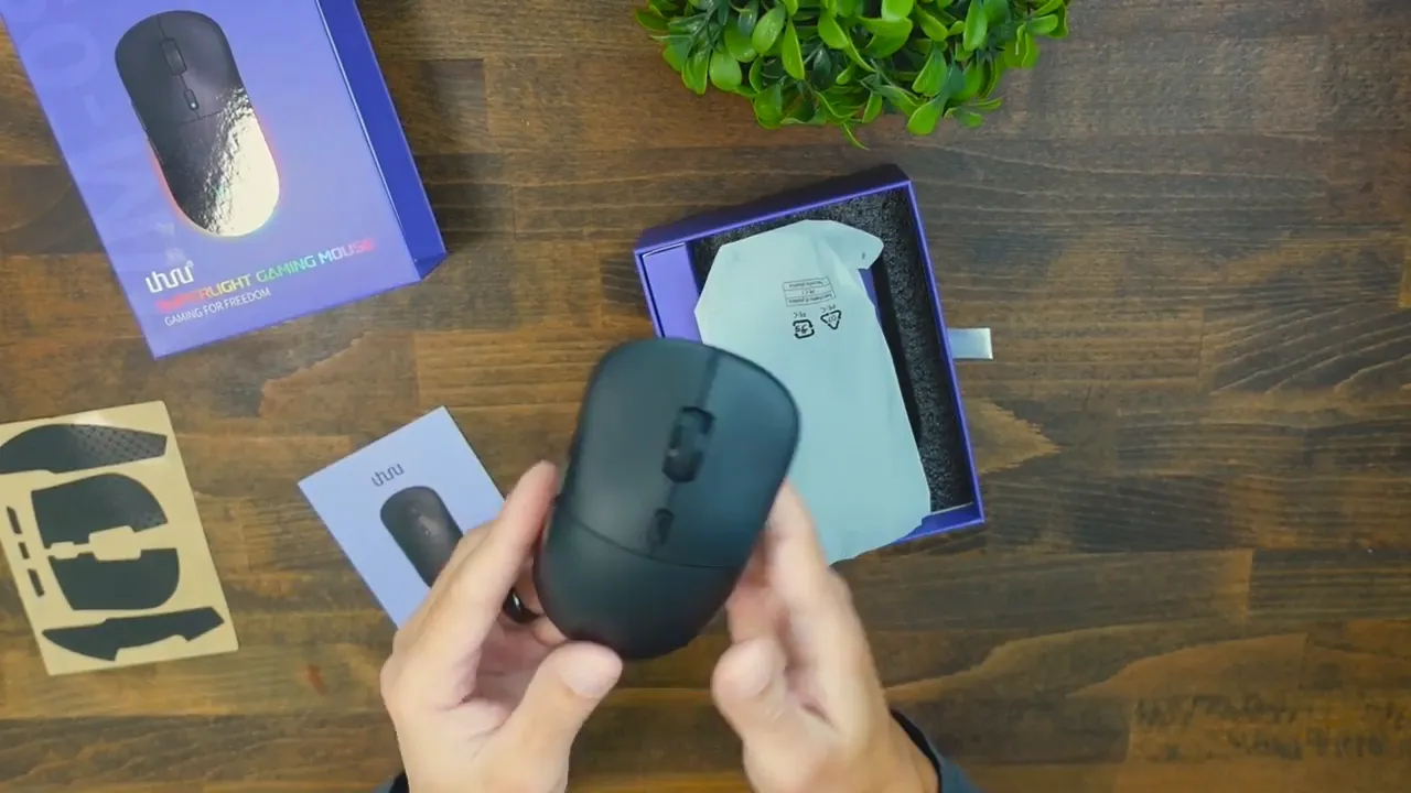 Uhuru WM-09 mouse held over opened box with manual and grip tape on table