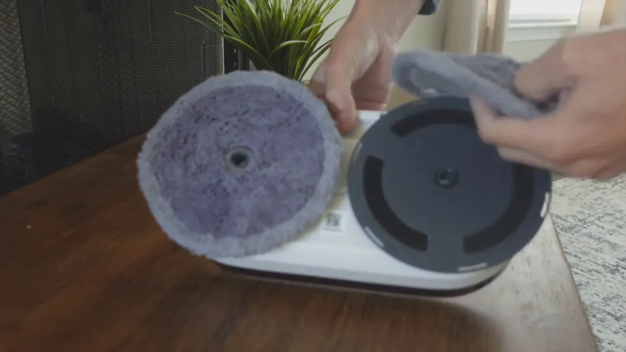 Person removing a round EVERYBOT Edge2 mop pad from the spinning mount, showing the pad and the empty mount