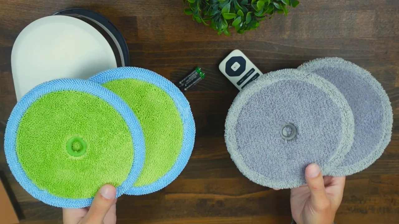 Four EVERYBOT Edge2 replaceable mop pads (two green/blue plush and two grey scrub) laid out with remote and batteries