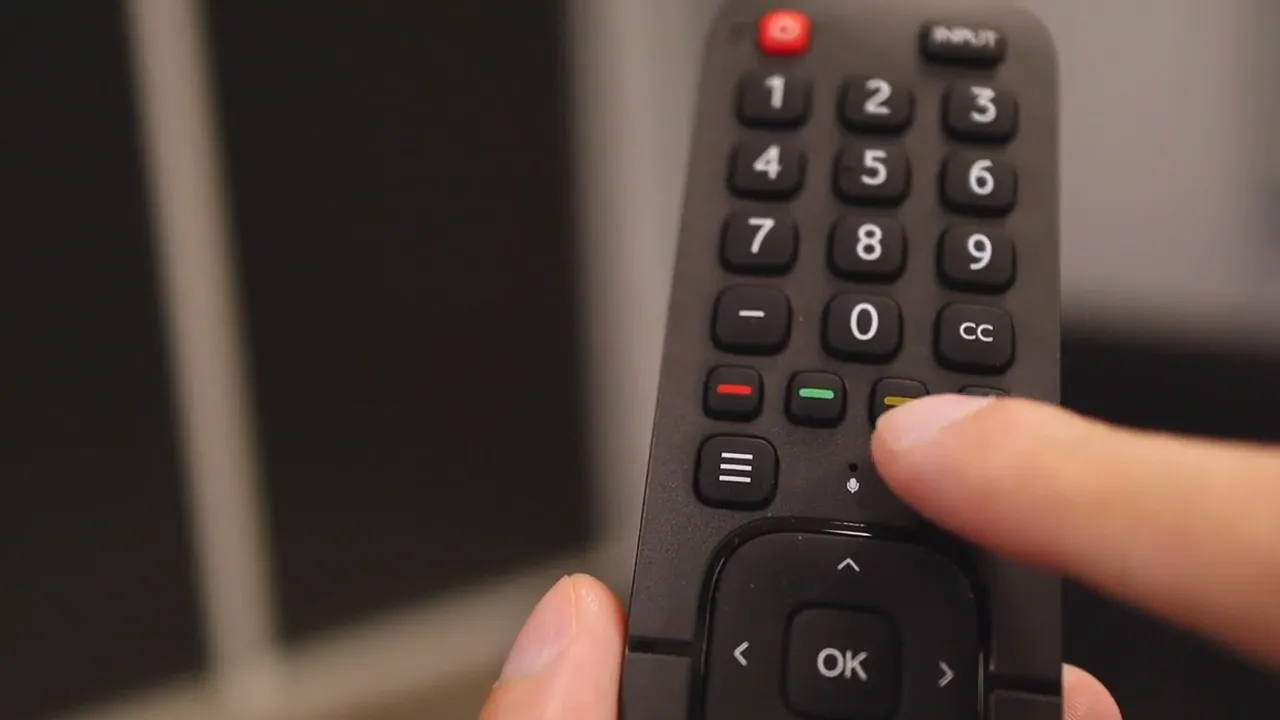 Close-up of the Hisense remote with a finger pointing at the Google Assistant microphone button
