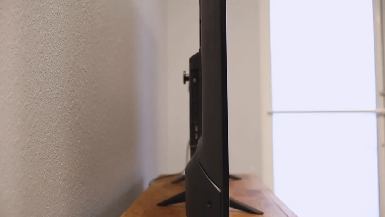 Side view of the TV on a wooden stand showing the screen profile and rear thickness