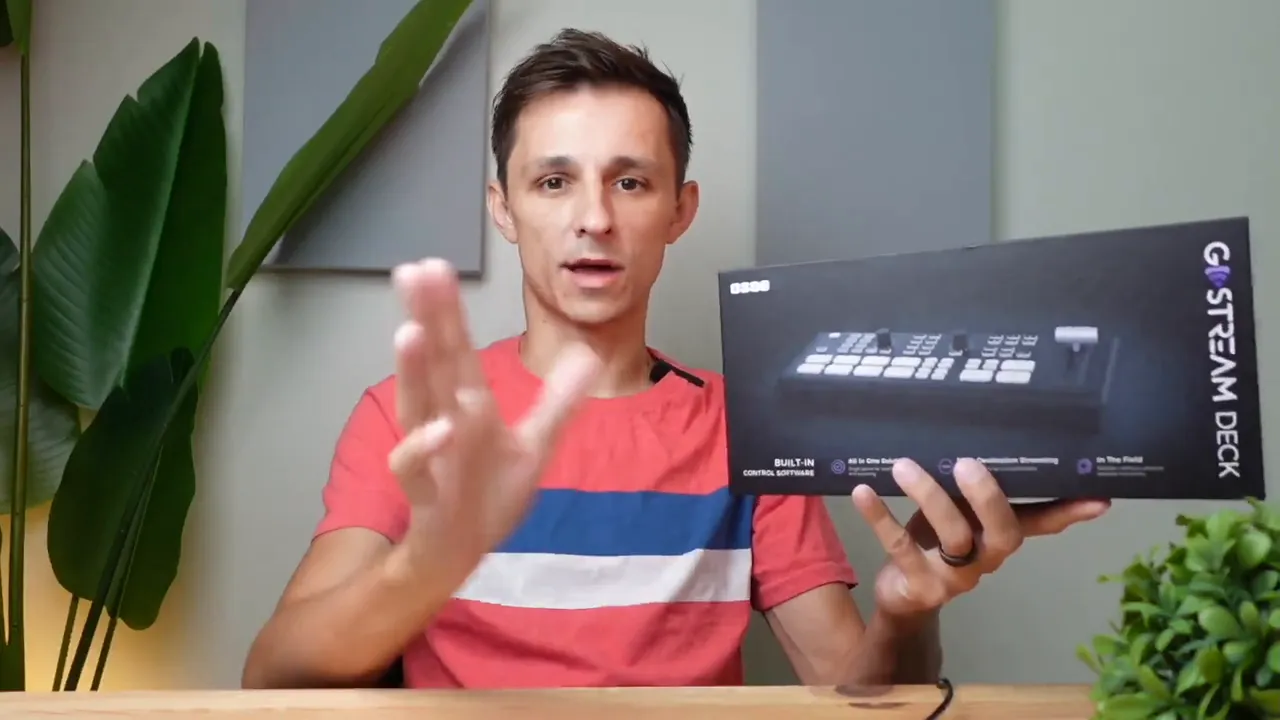 Presenter holding an OSEE GO‑Stream Deck retail box at a desk, showing the product packaging.