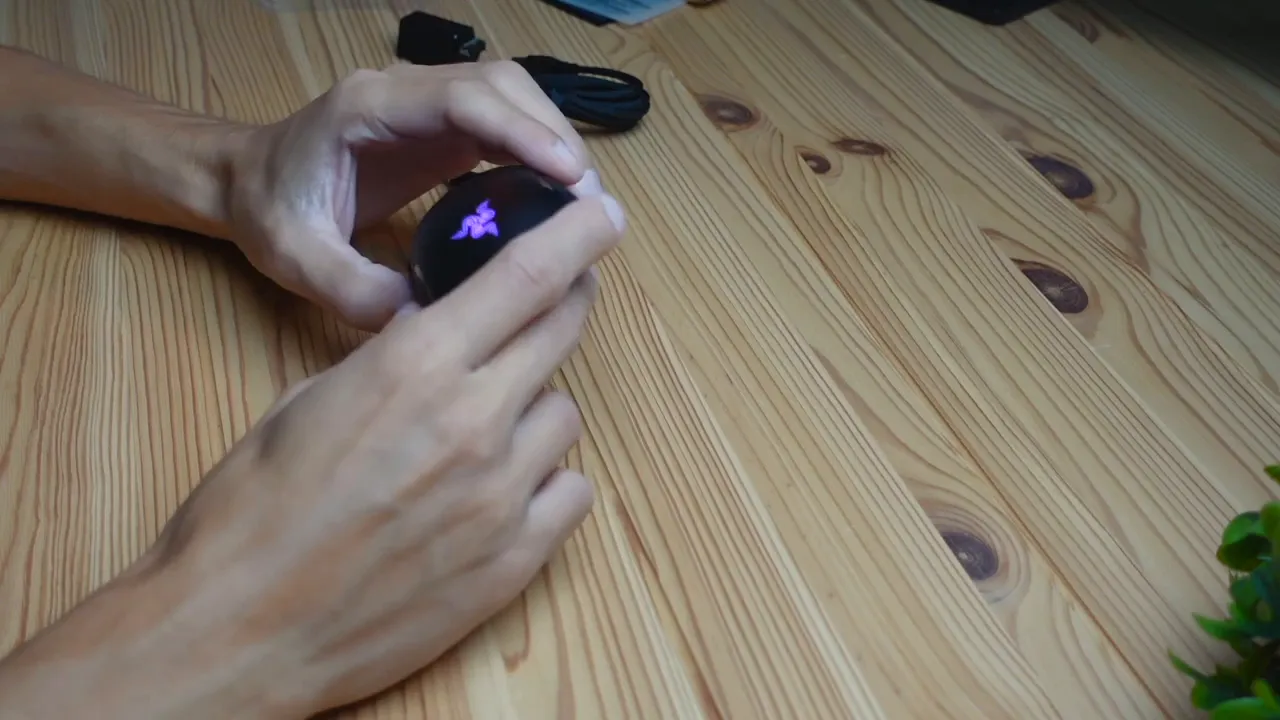 Close-up of the Razer Cobra Pro held in hands with the Razer logo illuminated purple, clearly showing the mouse's RGB lighting.