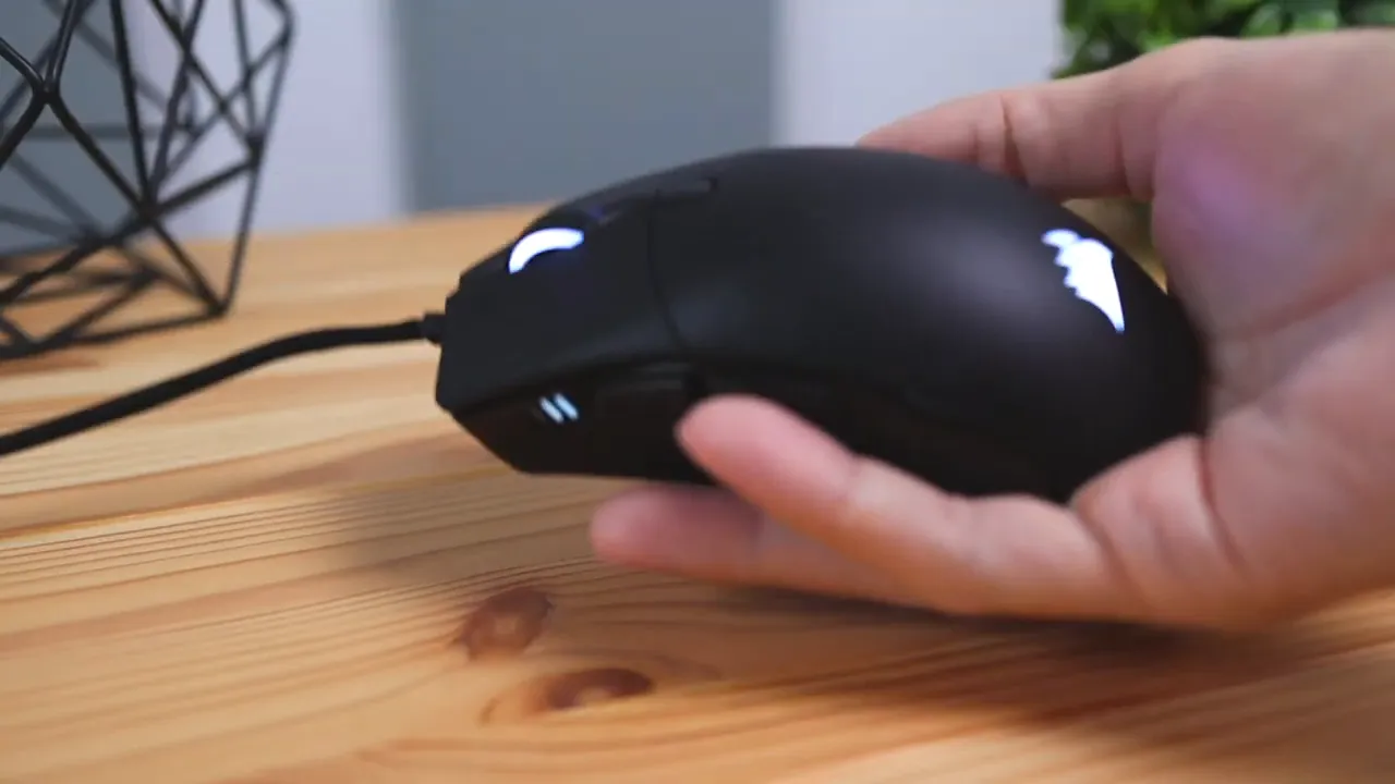 Corsair Sabre RGB Pro held in hand, showing the ergonomic shell, illuminated logo, side buttons and paracord cable.