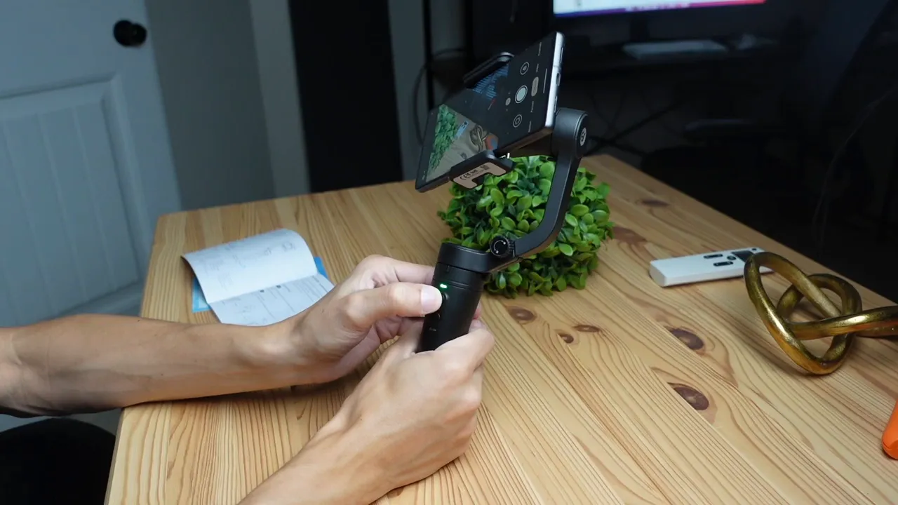 Hands pressing the power button on a FeiyuTech Vlog Pocket gimbal with the green LED illuminated