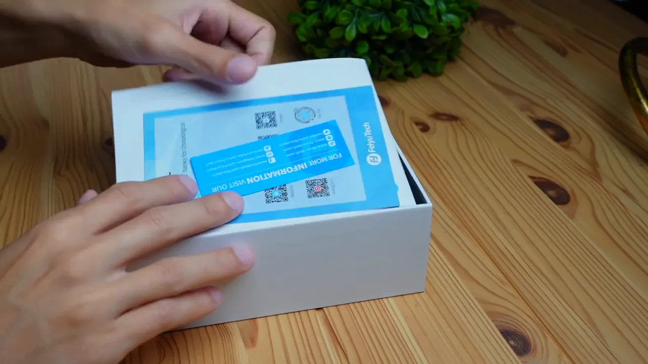 Hands opening the FeiyuTech Vlog Pocket box showing the instruction manual and paperwork inside