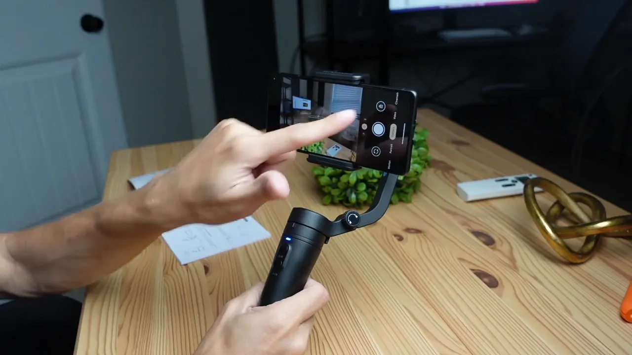 Hands using the FeiyuTech Vlog Pocket with a smartphone mounted, finger tapping the phone camera app to change orientation