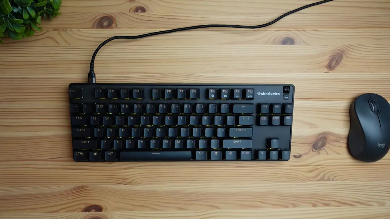 Clear top-down shot of the SteelSeries Apex 9 TKL keyboard and a mouse on a wooden desk showing the top-right volume dial and media control area.