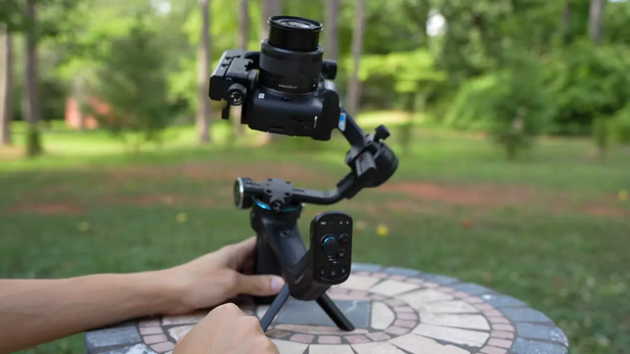 FeiyuTech SCORP‑C gimbal with camera mounted and hands holding the handle showing the joystick and controls