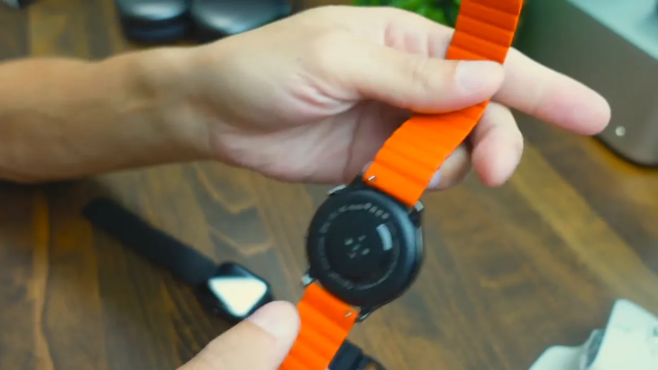 Hands holding an Imilab W13 round smartwatch showing the circular case back and bright orange magnetic strap