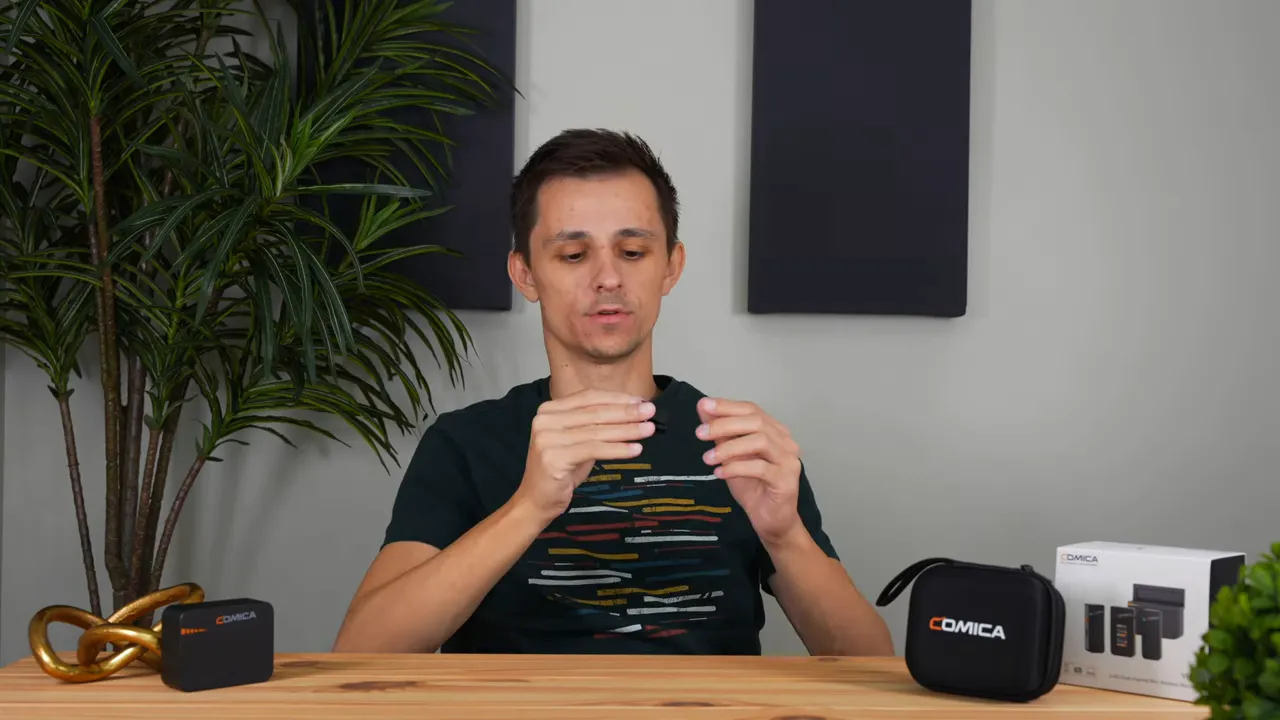 Presenter holding a Comica Vimo C3 transmitter with the charging case and product box on the table.