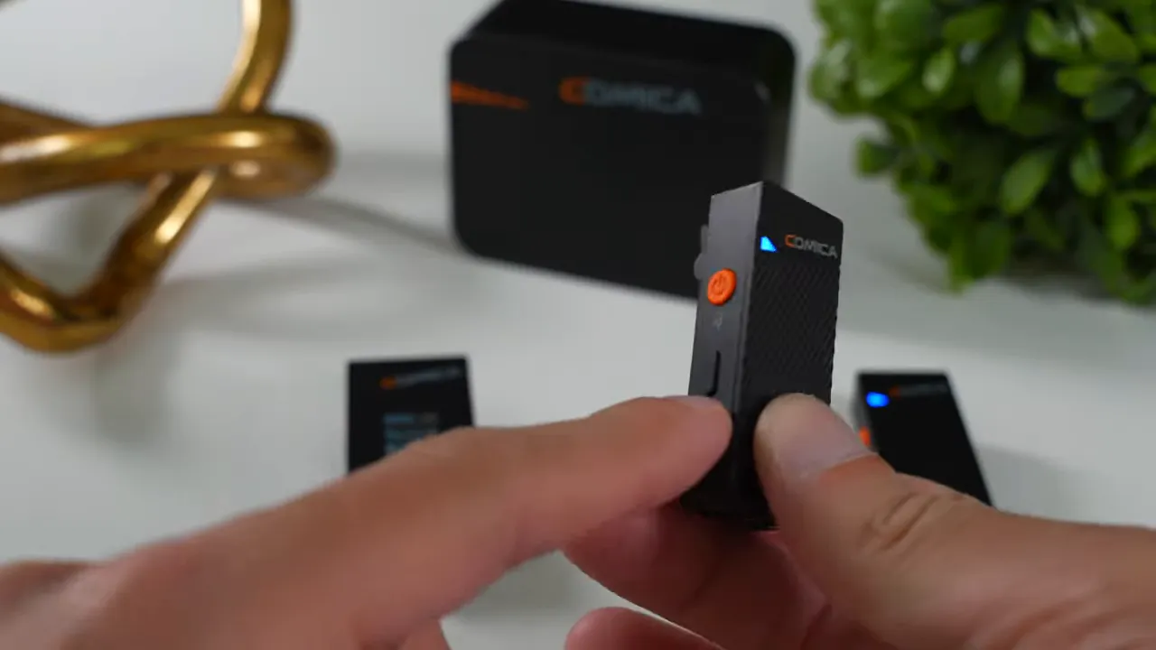 Close-up of a Comica Vimo C3 transmitter showing the orange power/mute button and side controls