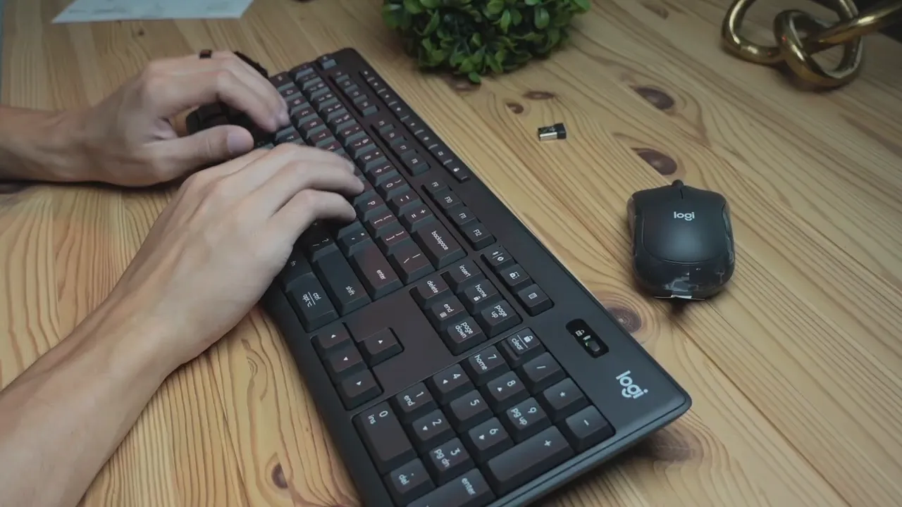 Overhead view of hands typing on Logitech MK370 keyboard with compact Logi mouse and USB receiver on wooden desk