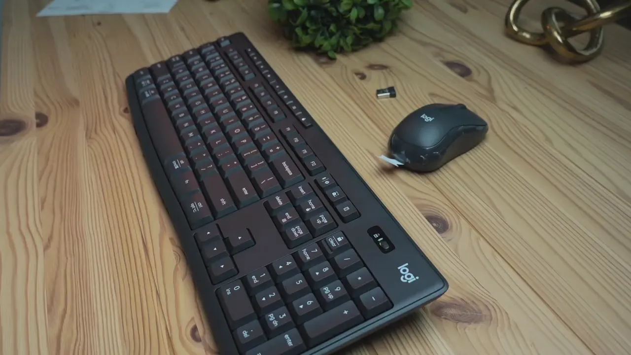 Angled view of Logitech MK370 full-size keyboard showing number pad and power switch with compact mouse and USB receiver on a wooden desk