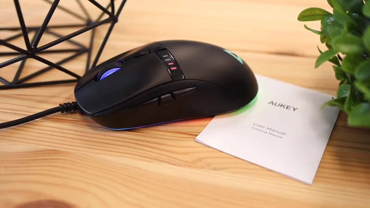 Black gaming mouse beside a white AUKEY user manual on a wooden desk