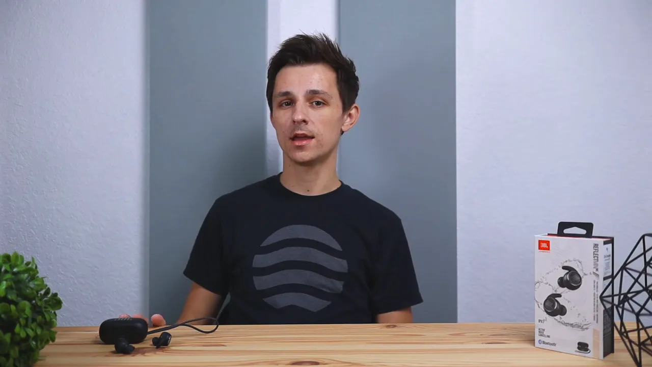 Neutral shot of reviewer with JBL Reflect Mini NC earbuds and charging case on the table and product box to the right