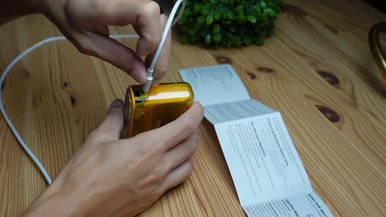 Hands inserting a USB-C cable into the charging port of a yellow transparent Starship Seer power bank on a wooden table.