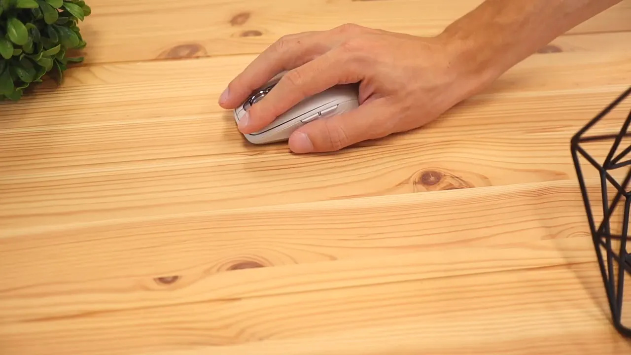 Hand resting on the small mouse in use on a wooden desk