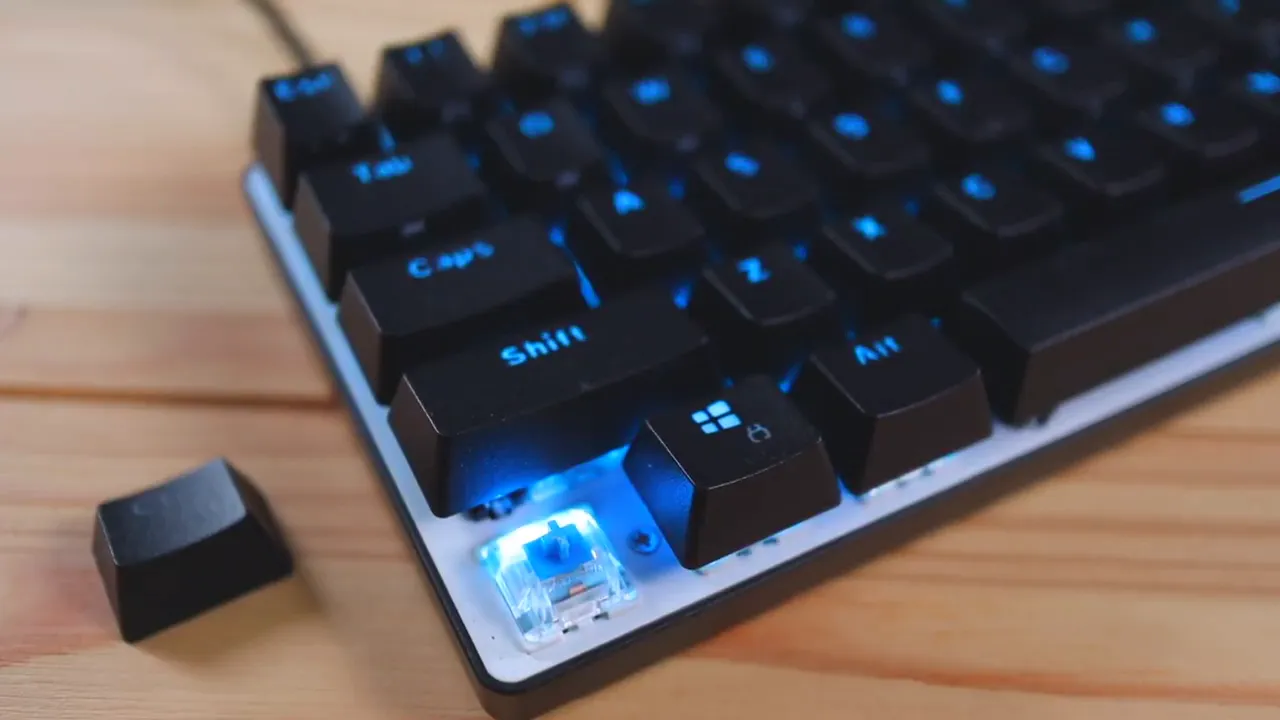 Keycap removed and placed beside the Atom keyboard revealing a blue Gateron switch and the white reflective backplate