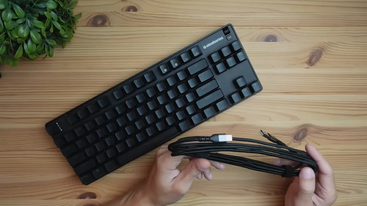 Top-down shot of the SteelSeries Apex 9 TKL with the braided USB-C to USB-A cable held in front showing the connectors