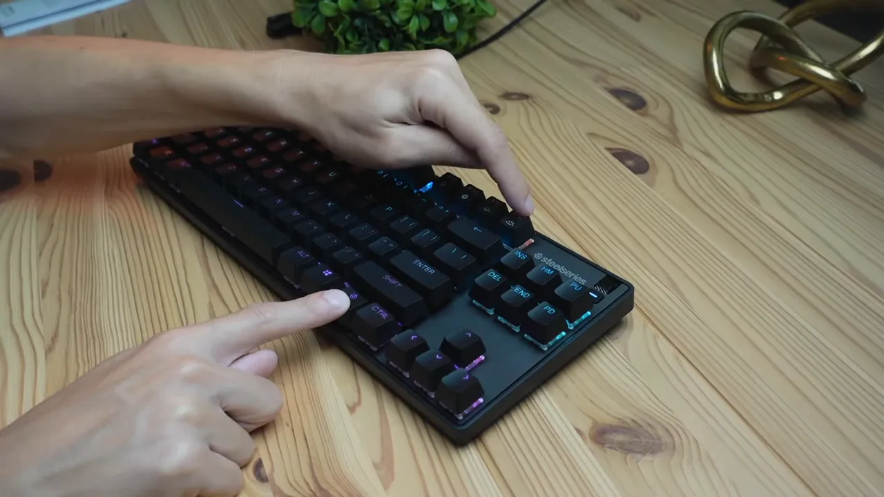 Close-up of a finger pressing the volume/brightness dial on the SteelSeries Apex 9 TKL with RGB lighting visible