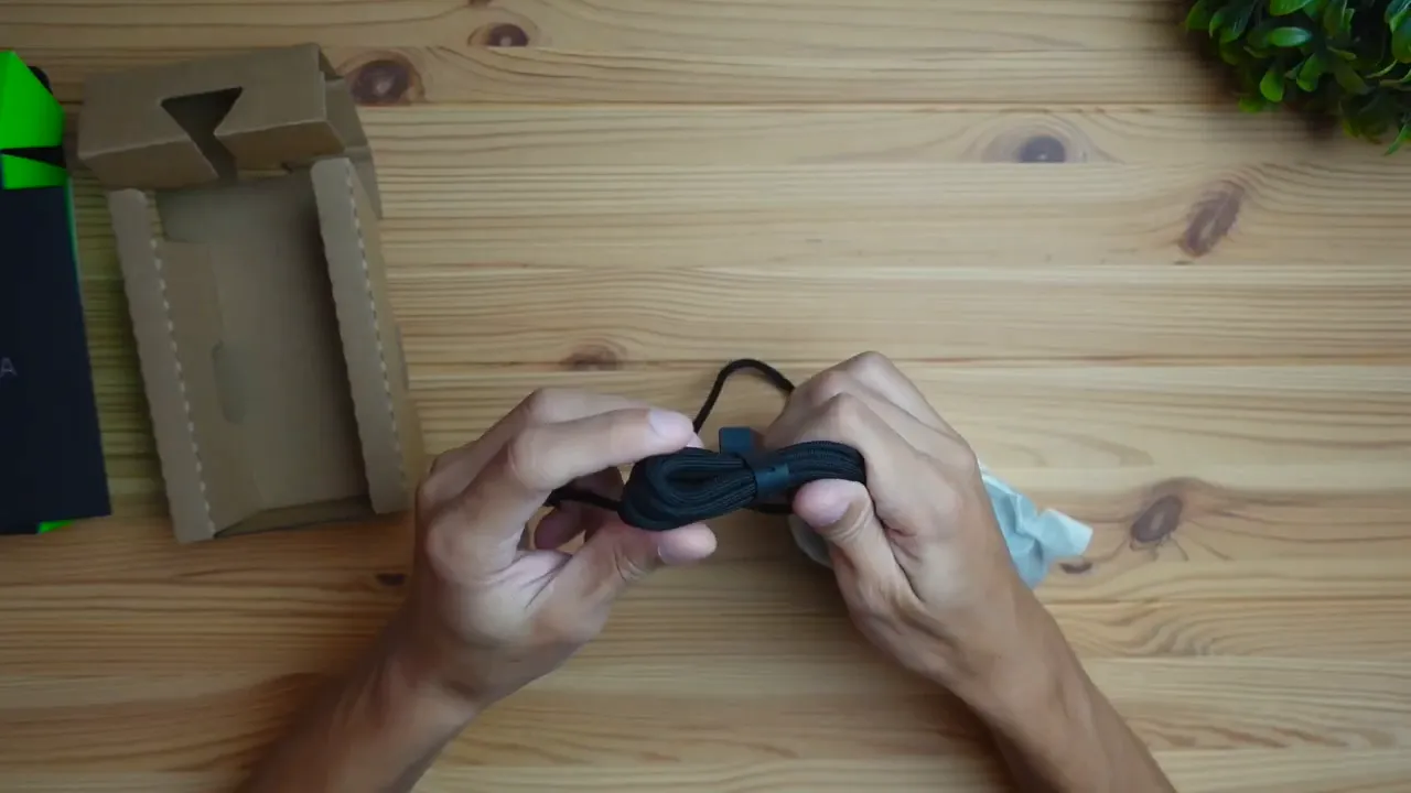 Coiled braided USB-A cable of the Razer Cobra mouse being examined during unboxing on a wooden desk
