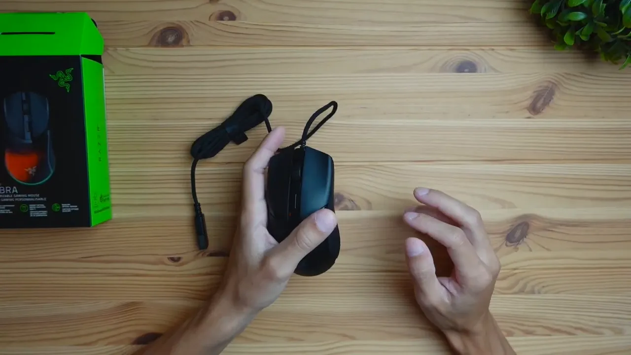 Top-down view of the Razer Cobra wired gaming mouse with braided cable and its box on a wooden desk.