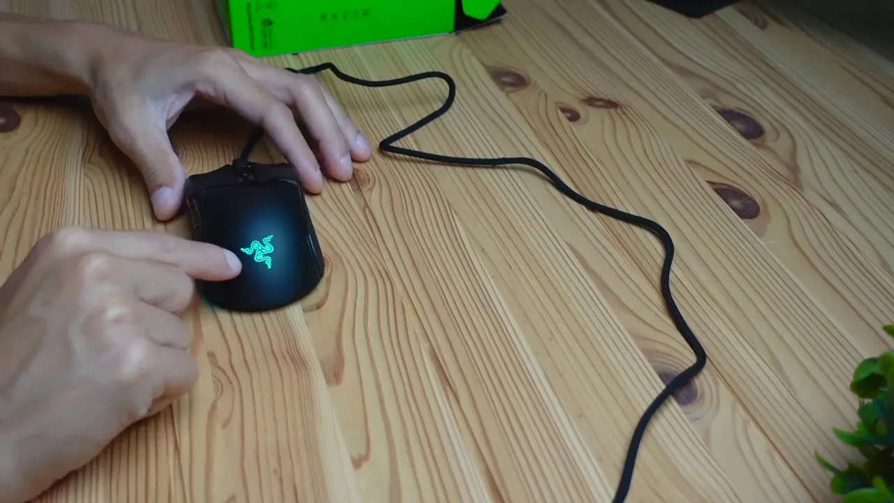 Close-up of Razer Cobra mouse with illuminated Razer logo and visible braided cable on wooden desk