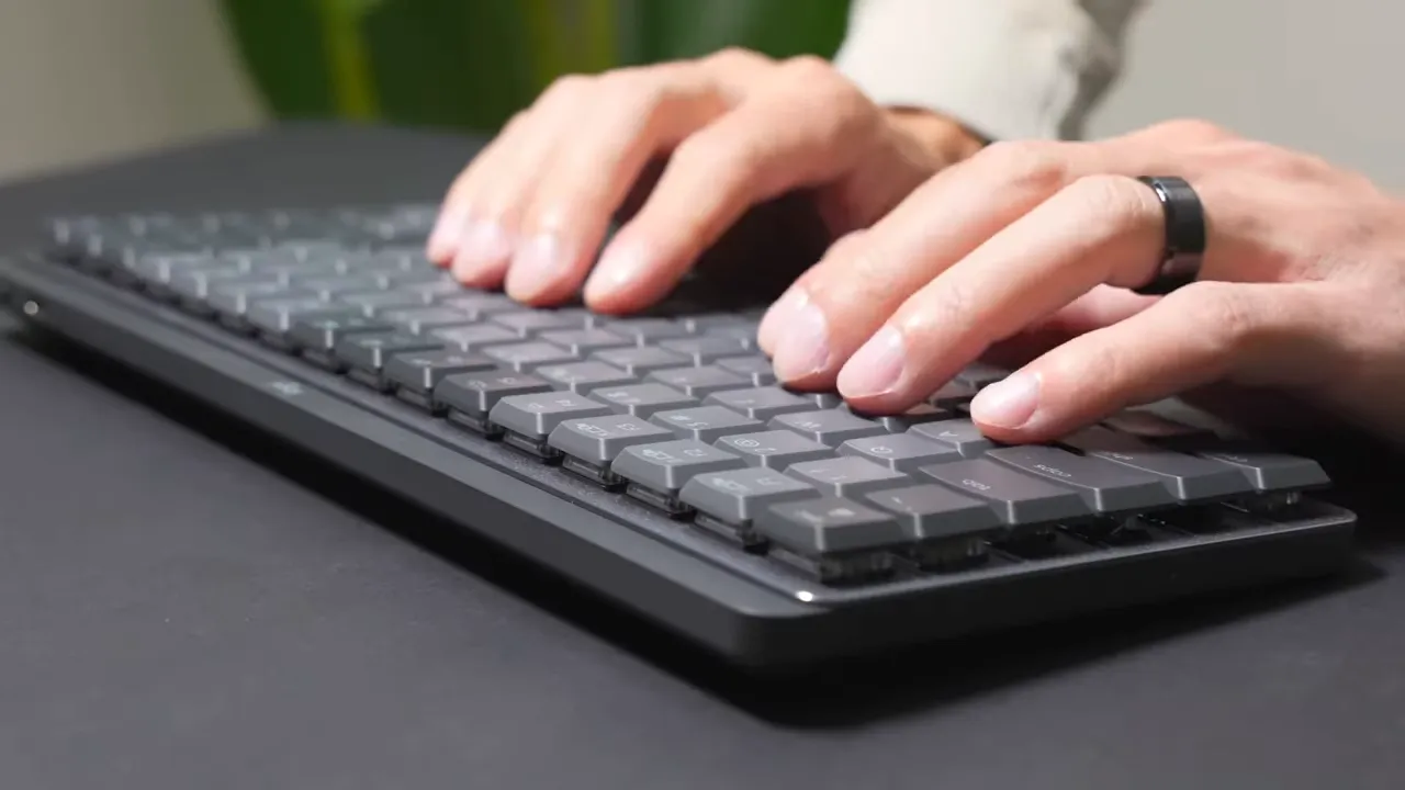 Side view of hands typing on the Logitech MX Mechanical Mini keyboard showing low-profile keycaps and finger placement