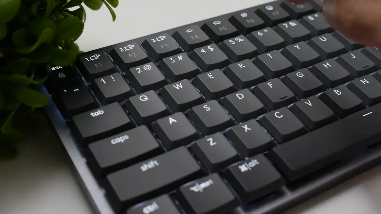 Wide close-up of MX Mechanical Mini keyboard showing white backlighting through key legends with a hand approaching