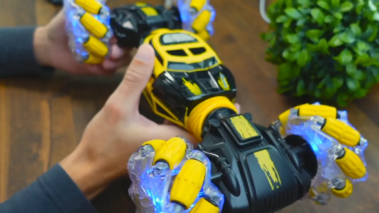 DoDoeleph RC car held in hands showing central chassis, yellow body panels and LED-lit mecanum-style wheels on a wooden surface