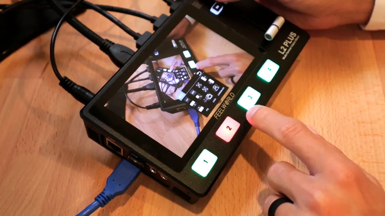 Close-up of Feelworld L2 Plus showing the T-bar, labeled input buttons and a finger pressing input 3