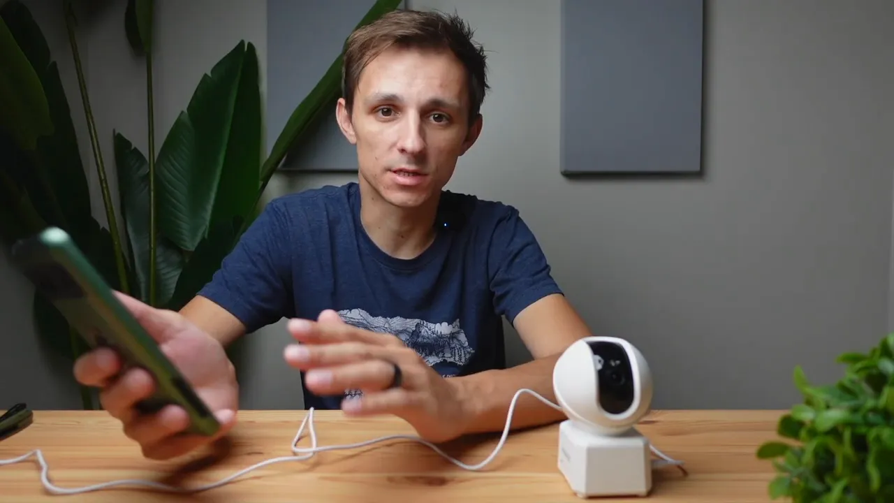 Person using smartphone and gesturing beside the Annke Creator Pro camera on a wooden table to demonstrate pan and tilt