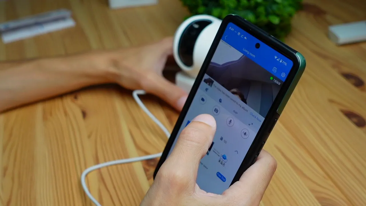 Smartphone showing Annke app live feed with a thumb tapping on on-screen control icons and Creator Pro camera in the background