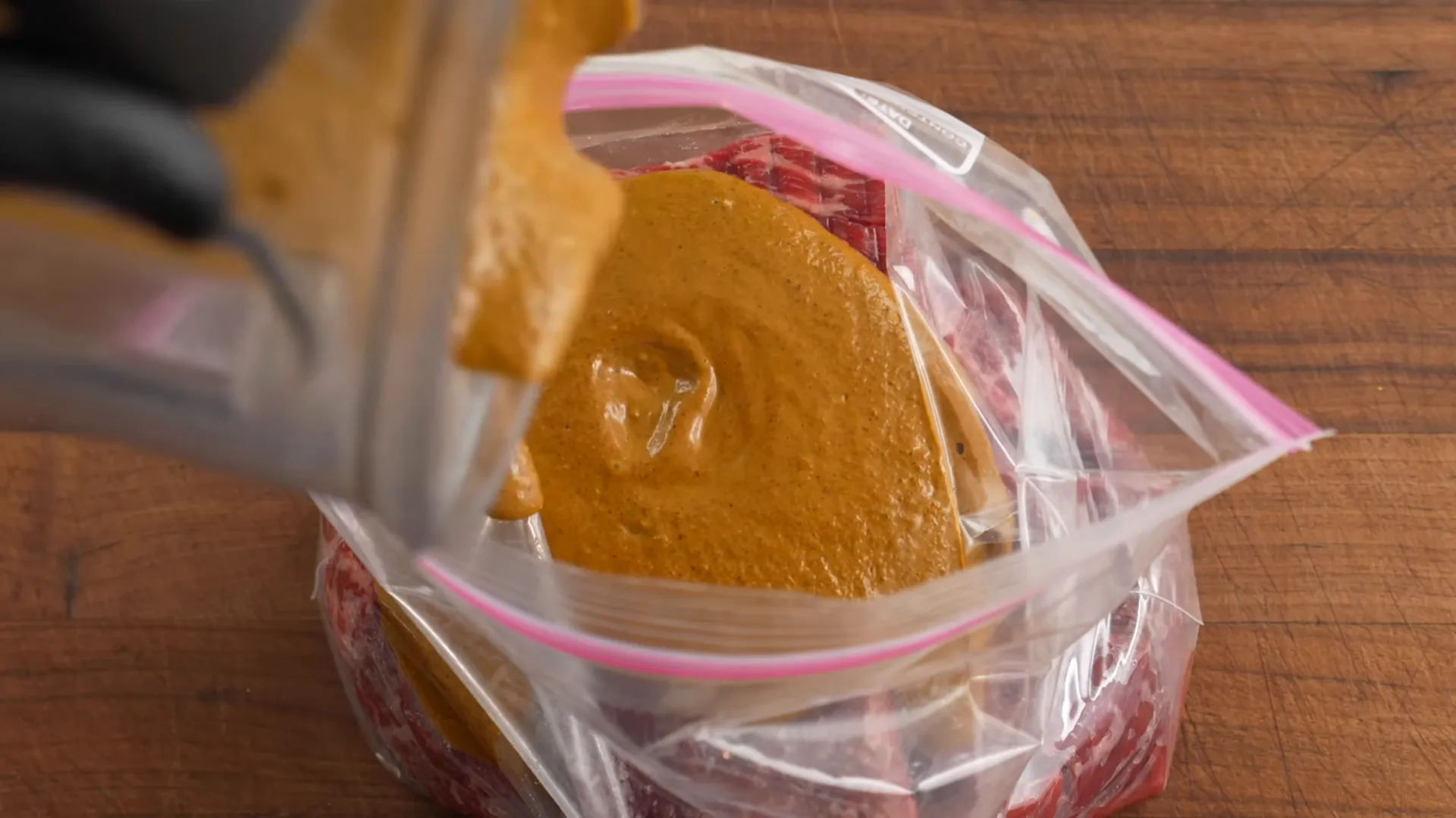Skirt steaks in a zip-top bag being coated in bright reddish-orange marinade