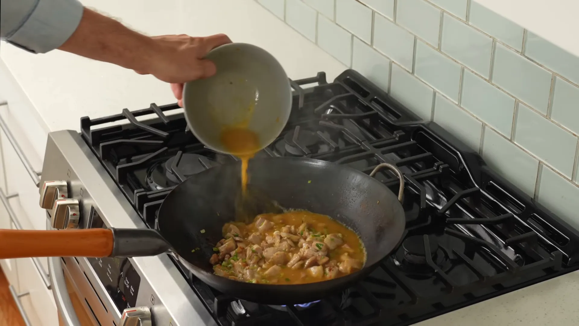 Pouring orange sauce around the perimeter of the hot wok