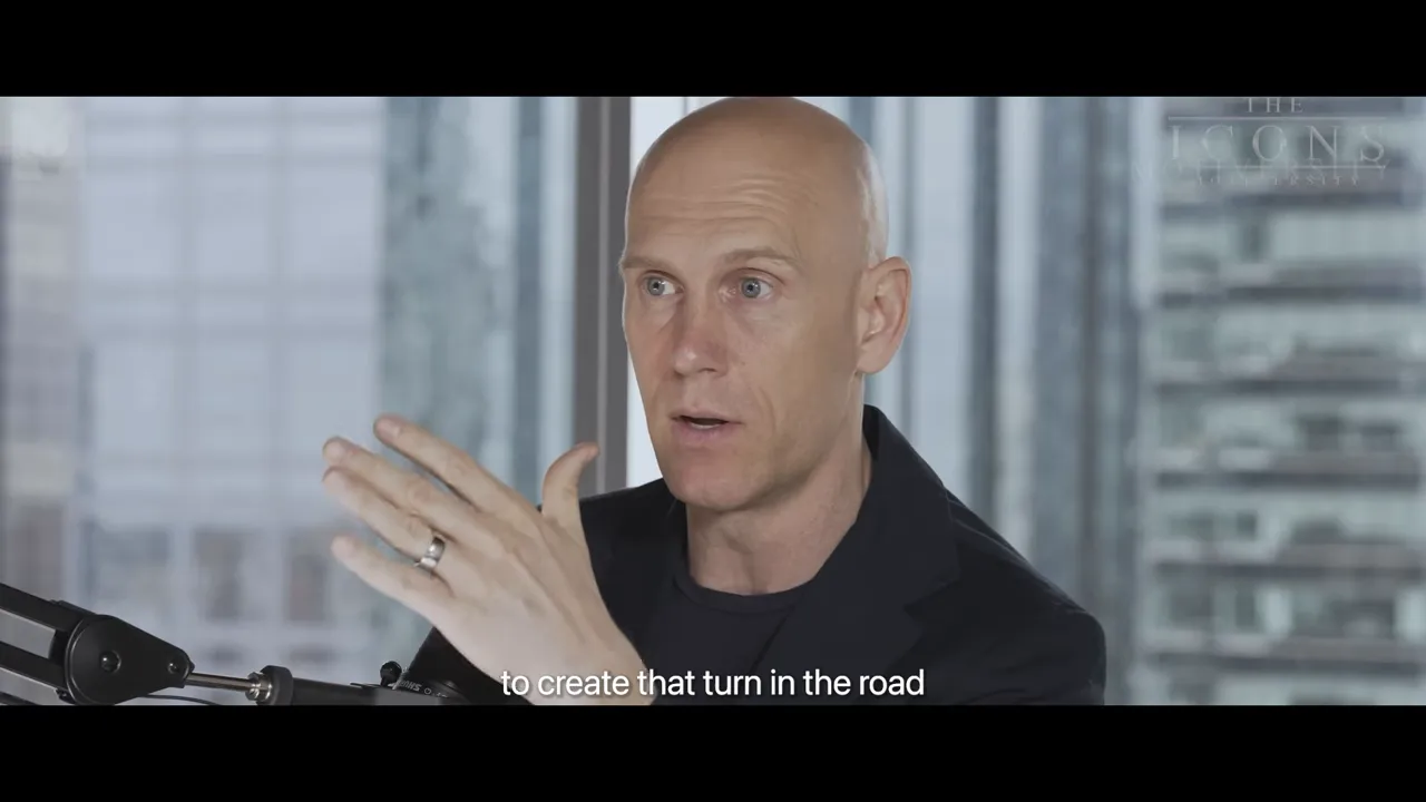 Close-up of a presenter gesturing into a microphone with the subtitle 'to create that turn in the road'.