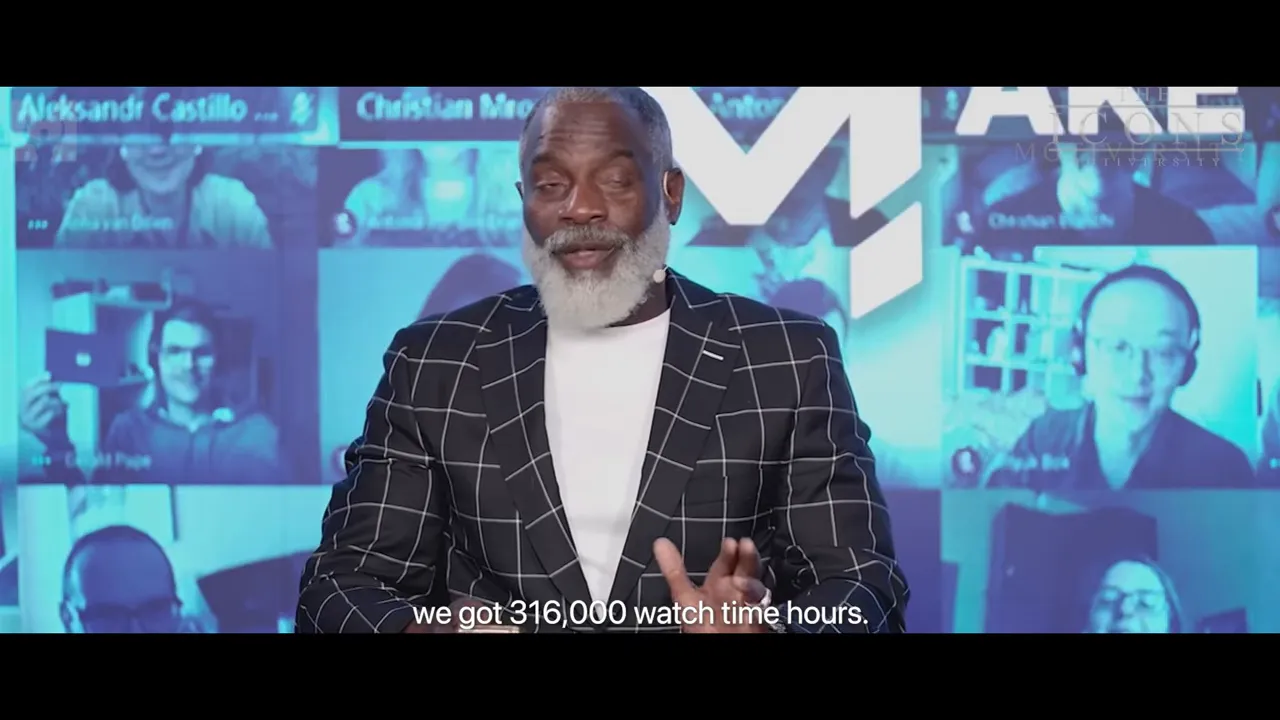 Presenter gesturing while speaking with a virtual audience backdrop; subtitle reads 