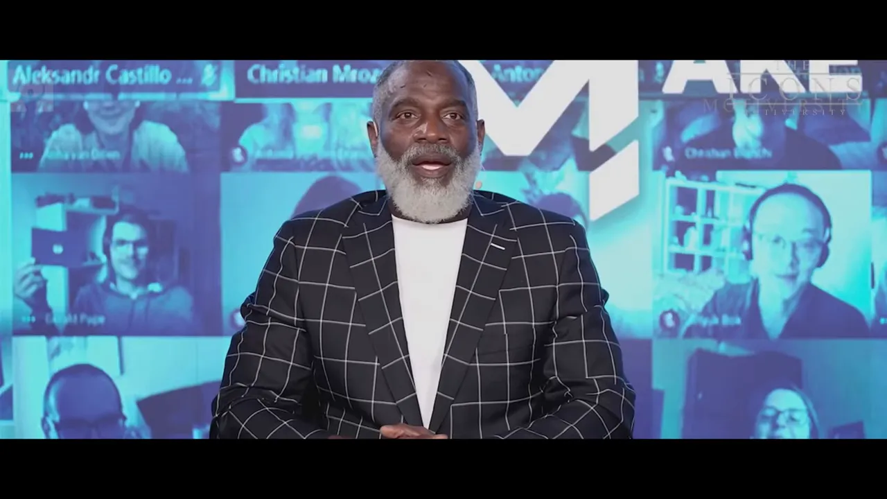 Presenter centered on screen with blue virtual-audience backdrop, wearing a checkered jacket