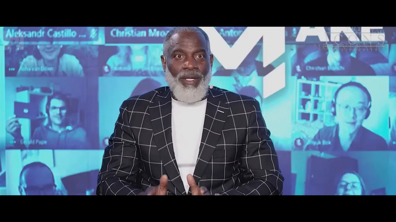 Presenter centered on screen in a checkered blazer with a virtual-audience tile background, speaking to camera.