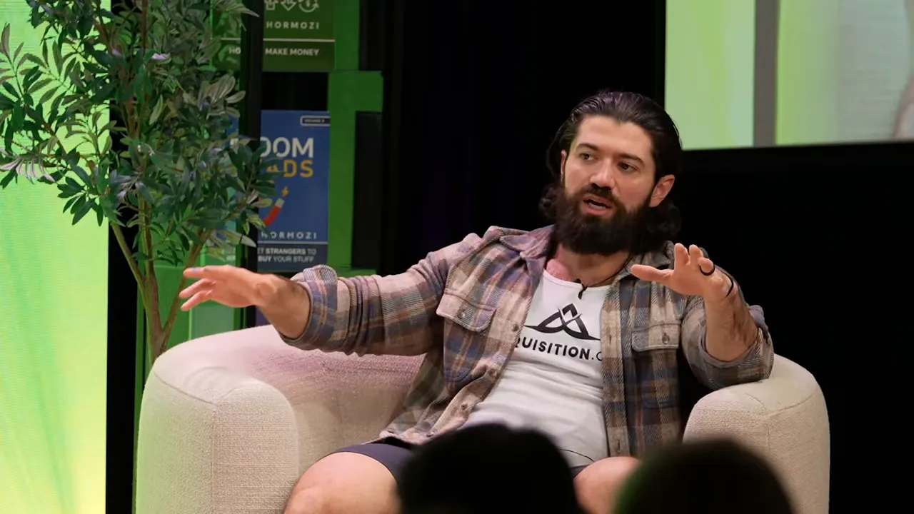 panelist on stage with open-handed gestures seated in a chair during a business panel