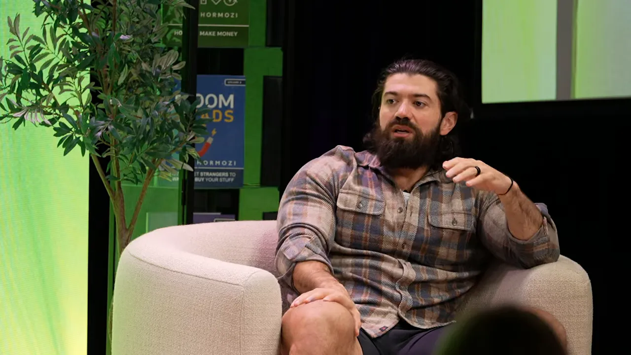 Speaker seated in an armchair gesturing to emphasize a point about CRM and scaling during a live talk.