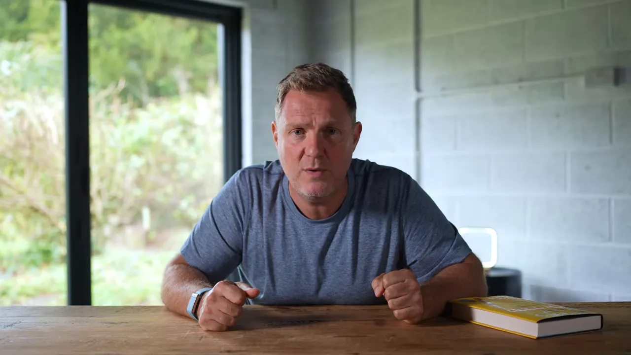 Presenter facing the camera at a wooden table with a book nearby, delivering a concise walkthrough.